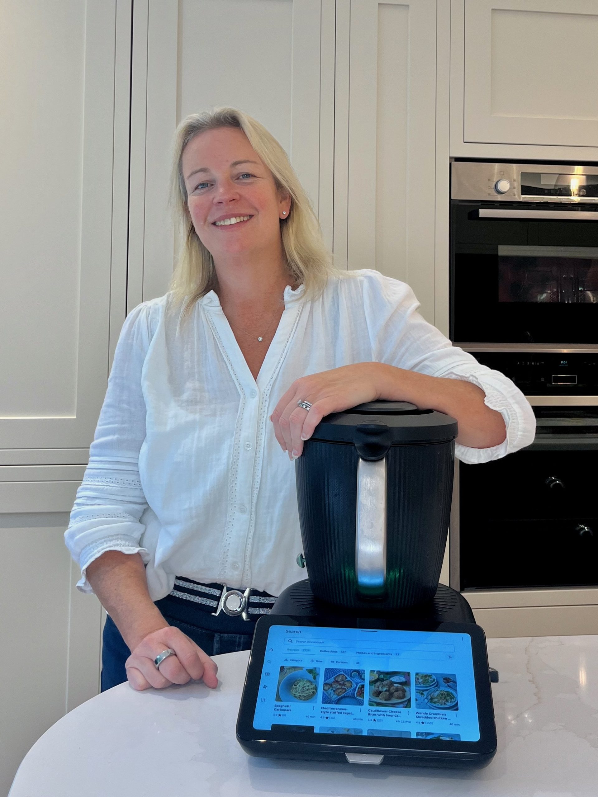 Alanah Light in a cream coloured kitchen resting her left arm on top of a black Thermomix®️ TM7..